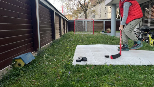 Young hockey player practicing wrist shots at home in a backyard on a shooting pad in front of a small net