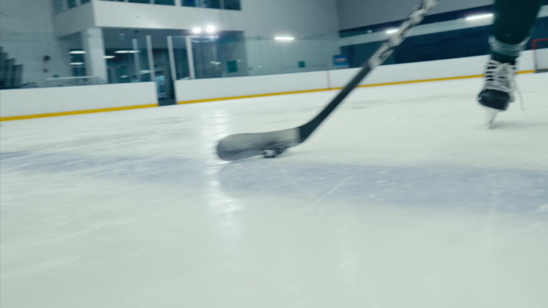 Close-up of a hockey stick blade handling a puck on the ice at a rink