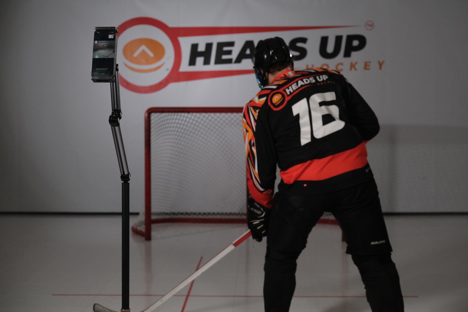 Hockey player taking a shot on a net beside a phone tracking stand